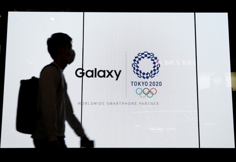 A passerby walks past an electric screen displaying logos of Tokyo 2020 Olympic Games and Galaxy at Galaxy Harajuku in Tokyo, Japan