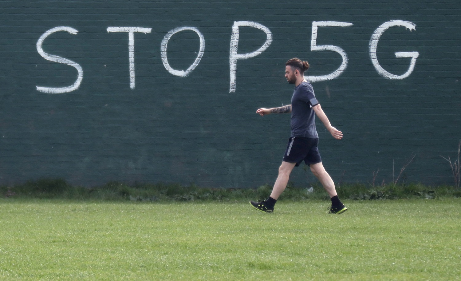 A man exercising during lockdown to combat an outbreak of coronavirus disease (COVID-19) walks past a graffiti that reads "STOP 5G" in London
