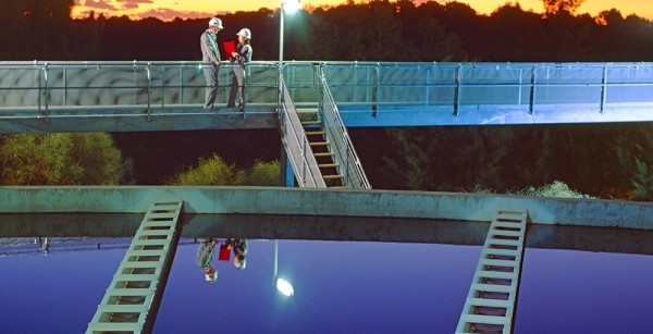 Scientists stand on a bridge over a collection tank at a wastewater treatment plant
