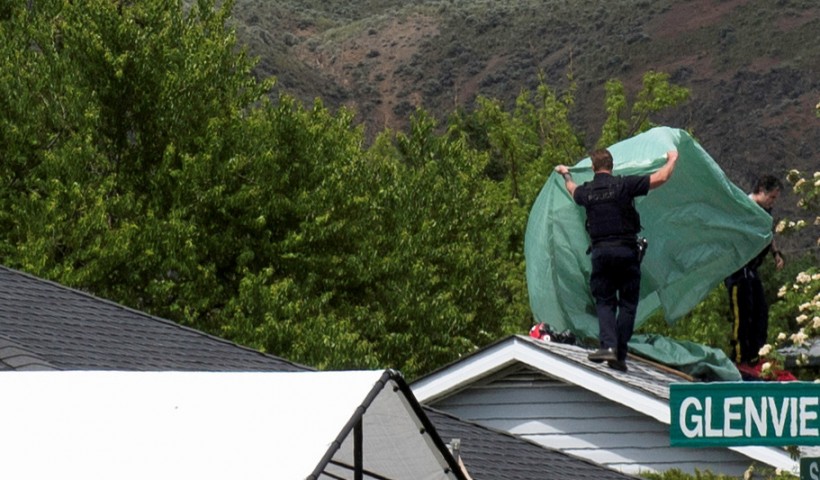 RCMP officers place a tarp over the roof of a house where a member of the Royal Canadian Air Force Snowbirds landed in Kamloops