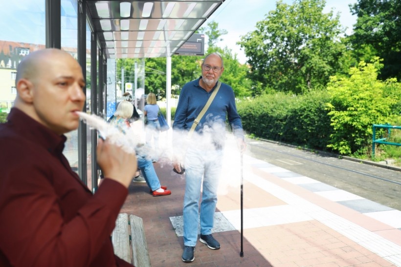 A man smokes a vape waiting for public transportation.