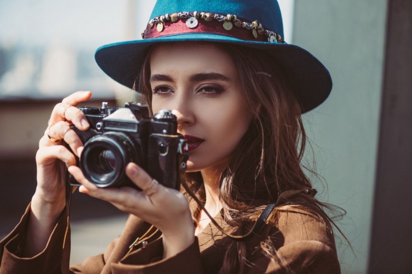 Elegant woman in hat taking photos on retro photo camera on roof