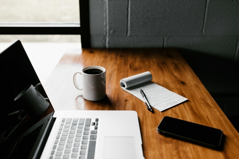 MacBook Pro, white ceramic mug, and black smartphone on table